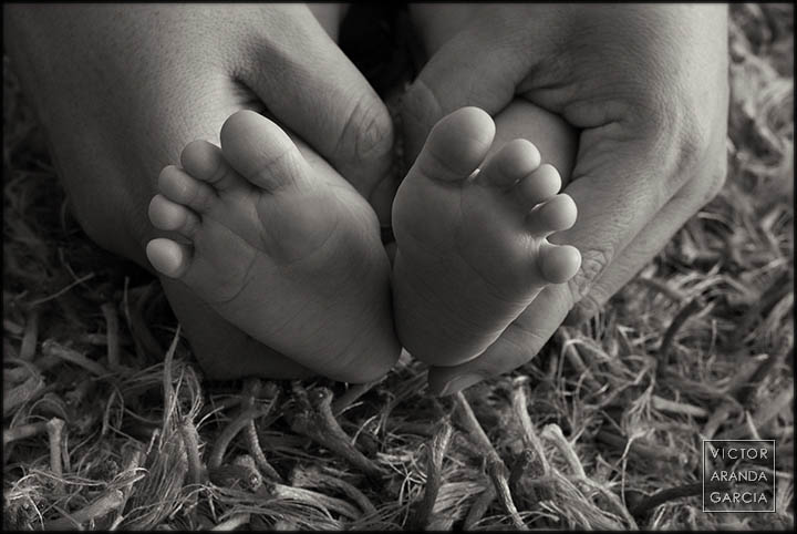 Fotografía artística de los pies de un recién nacido sostenidos por las manos de su madre sobre una alfombra
