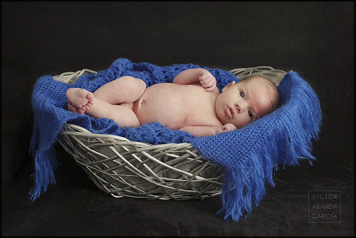 Fotografía de estudio de un bebé en una cesta con una tela azul